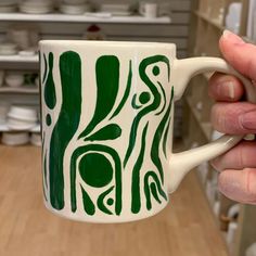 a hand holding a green and white coffee mug