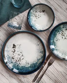 three blue and white plates with silverware on a wooden table next to each other