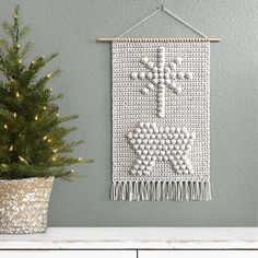 a crocheted wall hanging next to a potted christmas tree