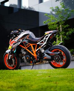 an orange and black motorcycle parked on top of a lush green field next to a building