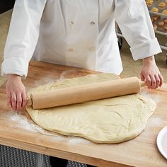 a person rolling dough on top of a wooden table