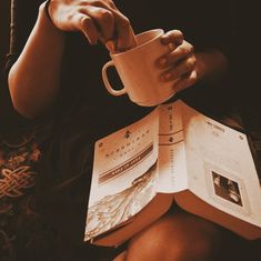 a person sitting down holding a book and cup