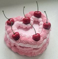 a pink cake with cherries on top is sitting on a white table and has three cherries attached to it