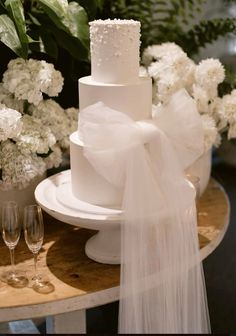 a white wedding cake sitting on top of a table next to wine glasses and flowers