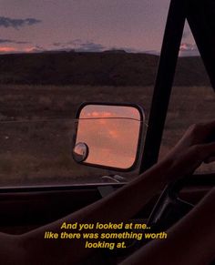 a woman driving in the back seat of a car at sunset with her hand on the steering wheel