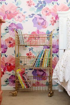 a gold metal book rack with books on it in front of a floral wallpaper