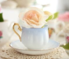 a teacup with a flower in it sitting on a doily next to cups and saucers