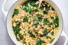 a pot filled with pasta and spinach on top of a table