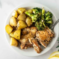 chicken, potatoes and broccoli on a plate with lemon wedges next to it