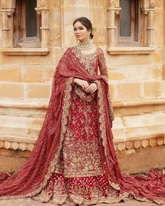 a woman in a red and gold bridal outfit standing on a stone walkway with her hands on her hips