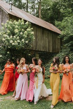 a group of women standing next to each other in front of a wooden building holding bouquets