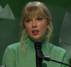 a woman with blonde hair and green dress standing in front of a microphone wearing earrings