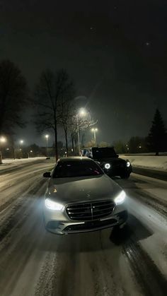 two cars driving down a snowy road at night