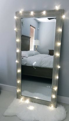 a mirror with lights on it sitting in front of a white fluffy rug and bed