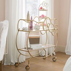 a gold metal shelf sitting in front of a window next to a chair and table