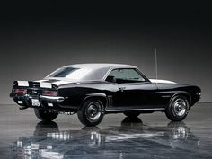 an old black and white muscle car parked in a dark room with the door open