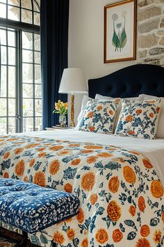 a bed with blue and orange bedspread in front of a brick wall next to a window