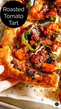 a person holding up a piece of roasted tomato tart on top of a pan