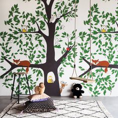 a child's room with a tree painted on the wall and toys hanging from it