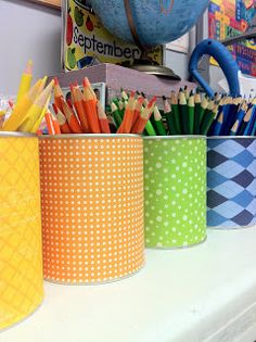 colorful pencils and markers are lined up in tins on a desk next to a globe