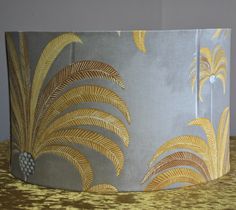 a yellow and grey lamp shade with gold leaf designs on it, sitting on a table