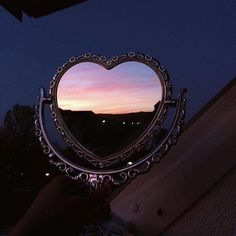 a heart shaped mirror sitting on top of a window sill in the night sky