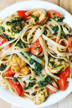 pasta with shrimp, tomatoes and spinach in a white bowl on a wooden table