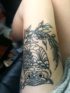 an owl tattoo on the arm with leaves and flowers around it's eyes is shown