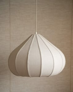 a white lamp hanging from a ceiling in front of a beige wall with vertical blinds