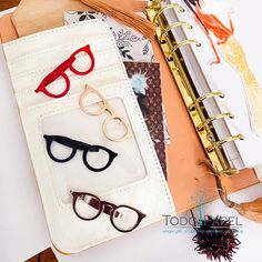 several pairs of glasses sitting on top of a binder next to an open notebook