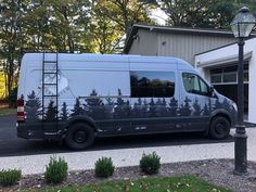 a van parked in front of a building with trees painted on it's side