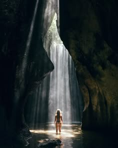 a woman standing in the middle of a body of water surrounded by rocks and sunlight