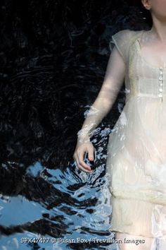 a woman standing in the water wearing a white dress