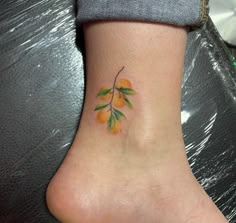 a small tattoo on the ankle of a woman's foot with oranges and leaves