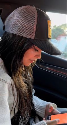 a woman sitting in the back seat of a car looking at her cell phone while wearing a hat