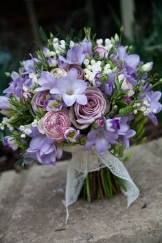 a bridal bouquet with purple and white flowers on a stone slab in the garden