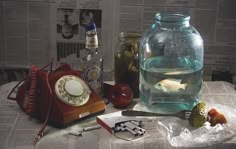 an old phone and other items are on the table next to a glass jar filled with water