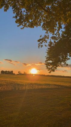 the sun is setting over an open field with grass and trees in the foreground