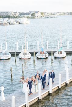 a group of people walking on top of a pier next to the ocean with boats