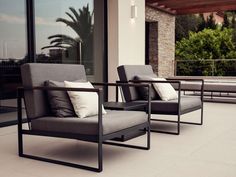 two gray chairs sitting on top of a patio next to a building with large windows