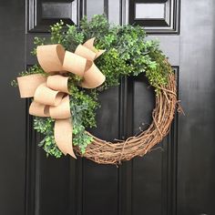 a wreath is hanging on the front door with burlocks and greenery around it