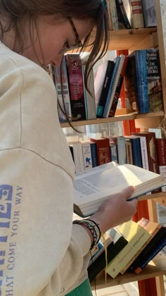 a woman is reading a book in front of a bookshelf