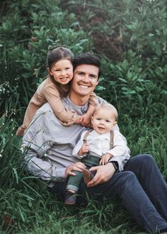 a man and woman are sitting in the grass with their little boy on his lap