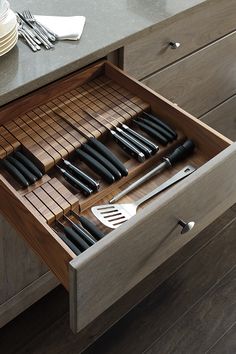 an open drawer with utensils and knives in it on a countertop next to plates