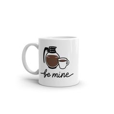 a white coffee mug with the words be mine on it and a cup of coffee next to it