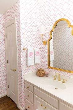 a bathroom with pink and white wallpaper, gold accents and a large mirror over the sink