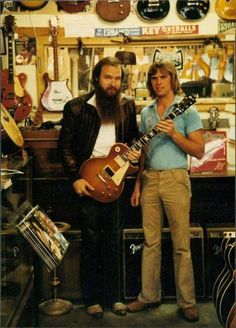 two people standing next to each other with guitars on display in the background and behind them there is a guitar