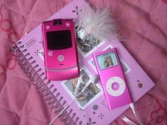 a pink cell phone sitting on top of a notebook next to an mp3 player and feather