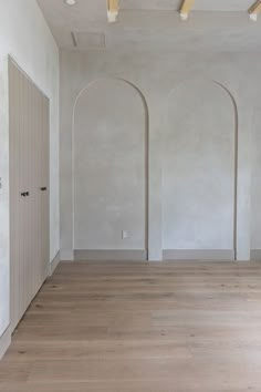 an empty room with white walls and wood flooring is pictured in this image, there are three arches on the wall