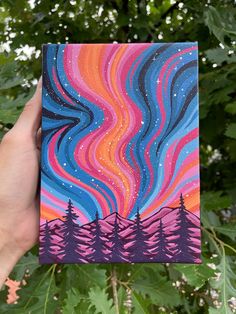 a hand holding up a colorful painting with trees in the background